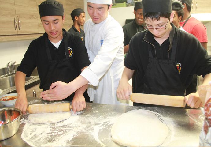 Des participants au programme Guys Can Cook roulent de la pâte à pizza avec un étudiant-chef du collège George Brown, au CSC Four Villages, en 2015.